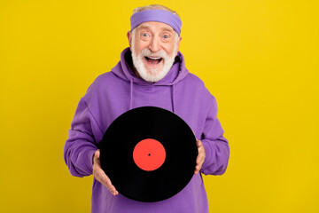 Photo of excited man pensioner good mood hold vintage vinyl disc isolated over yellow color...