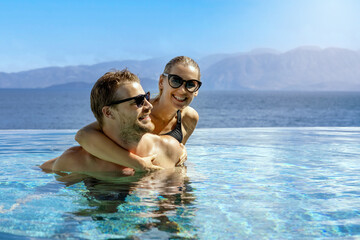 happy smiling young couple having fun together in infinity swimming pool. romantic summer vacation