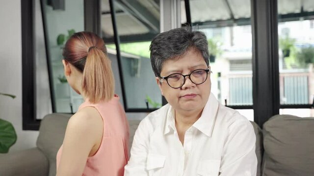 elderly mother and her daughter are sitting with their backs facing each other in anger and frustration
