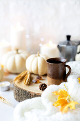 Cozy Fall setting with a cup of espresso coffee in a rustic cup, moka pot at the background with white pumpkins, autumnal leaves and burning candles.