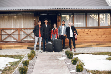 Group frinends with suitcases standing at wooden building