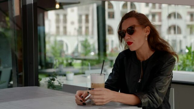 sexy lady with red lips and sunglasses is smoking in cafe, drinking latte, sitting alone and boring