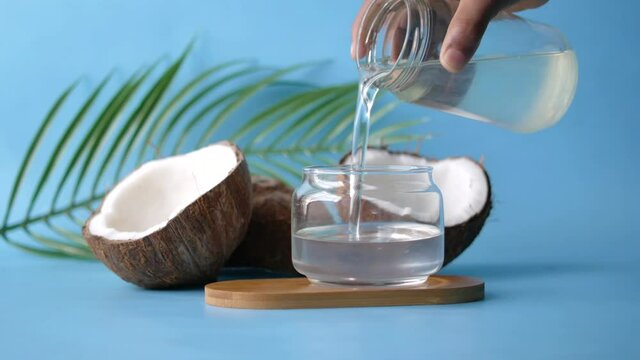 pouring coconut oil in a container on blue background 