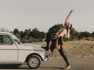 Shirtless hippie showing rock gesture near retro car