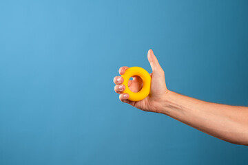 Squeeze, apply force. Soft toroidal rubber expander for the development of palm muscles in the male hand, blue background