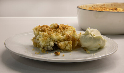 Sweet desserts. Apple crumble slice of cake with cream on a white dish in the kitchen table.	
