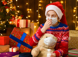 Child girl as Santa helper posing in new year decoration. Wearing a protective face mask against...