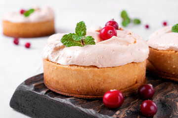 Small meringue pie with fruit and berry curd on shortcrust pastry served on the wooden board. Portion sized dessert