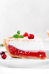 Meringue pie piece with berry jam on shortcrust pastry served on the white plate. Exquisite dessert