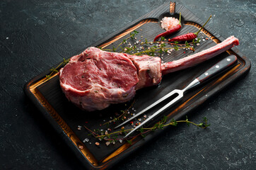 Dry aged raw tomahawk beef steak with ingredients on a black stone background. Top view. Flat Lay.