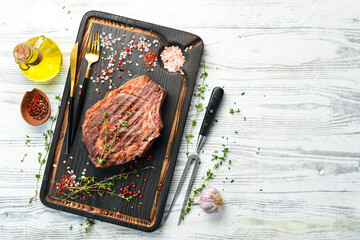 Grilled beef steaks with spices on a white wooden background. Top view, free copy space.