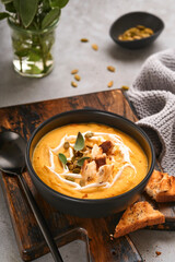 Pumpkin traditional soup with creamy silky texture with sage leaves and red pepper in black plate or bowl. Old grey background. Copy space. Mock up. Top view, flat lay.