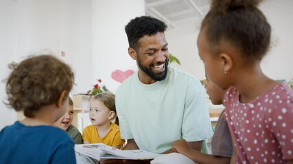 Group of small nursery school children with man teacher on floor indoors in classroom, reading book. - Powered by Adobe