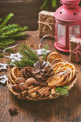 Dry orange, star anise, cinnamon, pine cones and fir tree in rustic plate on wooden table. Homemade...