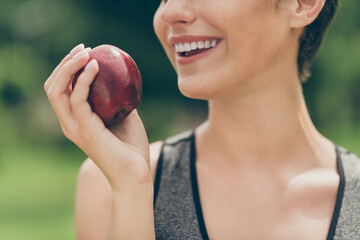Cropped photo of positive pretty sportswoman eat natural apple wear grey top nature park garden...