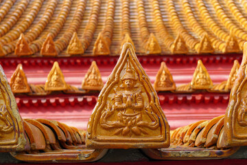 Close-up of traditional Thai roof tile in orange color with Buddhist gods carved on triangular tiles