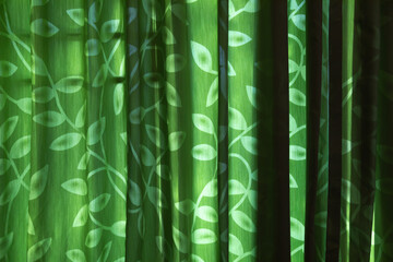 Green curtains with leaf motifs shine from outside the room with interesting shadows. For background.
