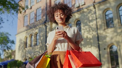 Happy African American woman with shopping bags using phone, mobile shopping
