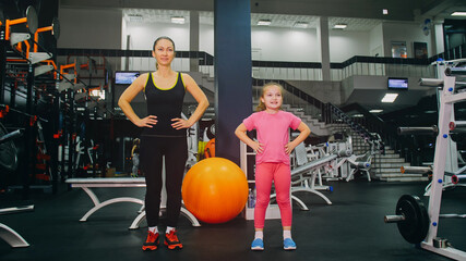 Mother and Daughter in the Gym, Family Performs Physical doing Exercises Fitness, Healthy Lifestyle. Happy Sports Family Training Concept. Woman with her Child doing Stretching Warm-up in the Gym