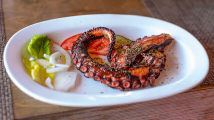 baked octopus tentacle with onions and herbs in a white plate . in the cafe of the island of Crete