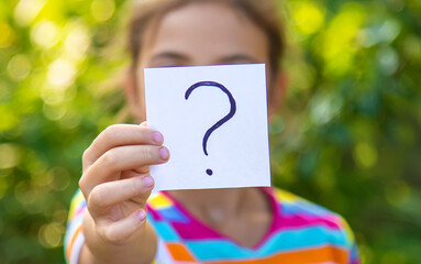 The child holds a paper with a question mark. Selective focus.