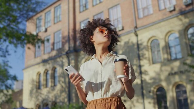 Stylish young woman walking in the city with smartphone and coffee, tourism