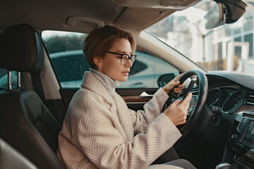 attractive stylish woman sitting in car dressed in coat