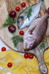 Uncooked Sea Bream fish on round wooden cutting board with cherry tomatoes, onion and spices. Food top view photo. Healthy eating concept. 