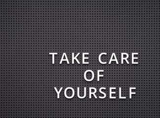 Words Take Care of Yourself spelled out with white letters on gray pegboard.
