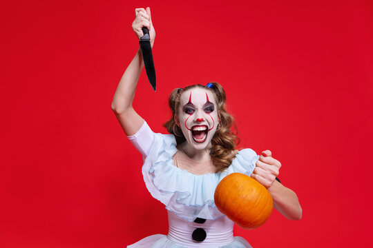 Halloween spooky theme. Mystical blonde girl with bright holiday make up holding knife isolated over red background