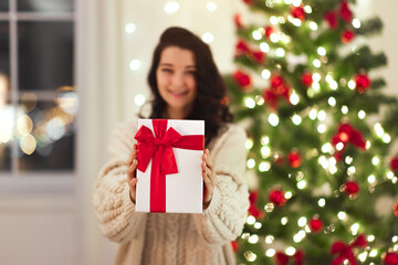 Obraz na płótnie Canvas Time for gifts, gift box in girl's hands. Selective focus of female hands giving present in the gift box to camera during Christmas celebration in the room at home. Marry Christmas and Happy Holidays