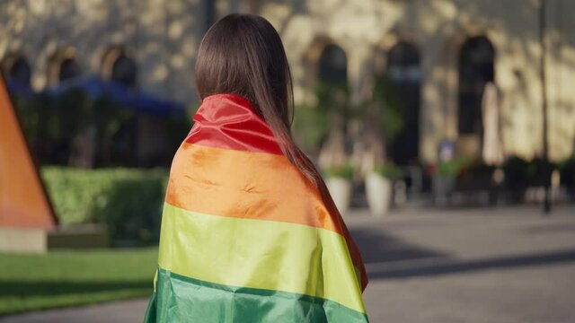 Brunette woman wrapped in rainbow flag standing in park, lgbt rights movement