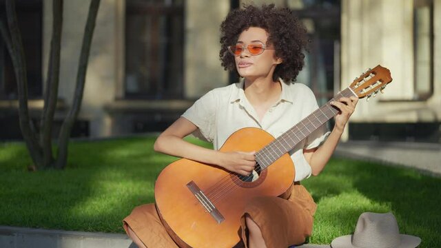 Smiling curly-haired street performer playing acoustic guitar and singing, hobby