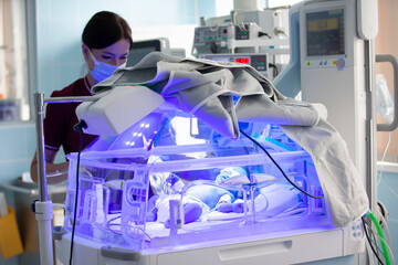 A newborn baby is treated for jaundice under ultraviolet light in an incubator. Department of neonatal resuscitation, intensive care unit for premature newborns. - obrazy, fototapety, plakaty