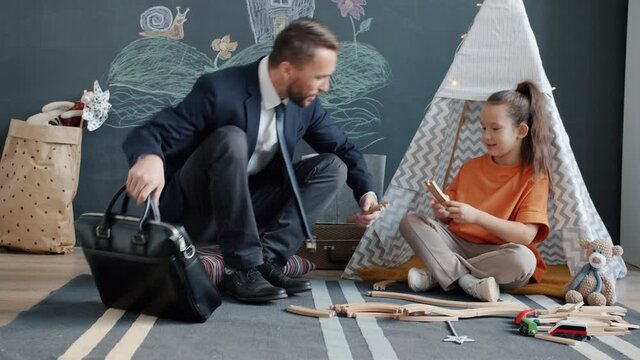 Loving ather young cheerful businessman is coming home talking and playing with little daughter bonding indoors in cozy apartment.