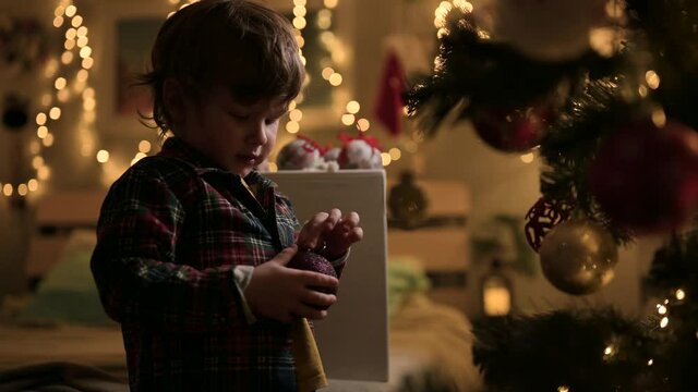 Christmas tree. A little boy at home at night plays with Christmas decorations, broke the Christmas ball. The mischievous kid does not obey his parents.