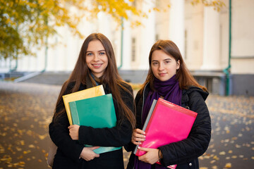 Two female students with learning materials near university building. Cool October morning in University campus