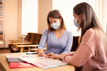 Fototapeta premium Two students in protective medical masks working together in library, preparing for classes. Conventional education during coronavirus pandemic
