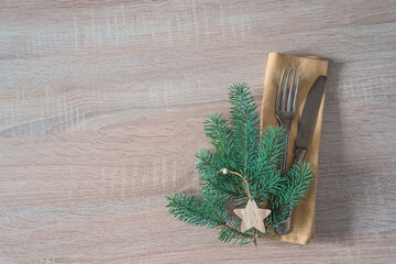 Place setting for christmas holiday dinner; Vintage fork and knife on linen napkin and fir twig and wooden christmas decoration on wooden background; space for text
