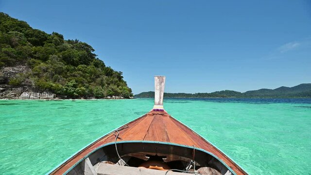 Wooden long-tail boat sailing on emerald tropical sea at lipe island