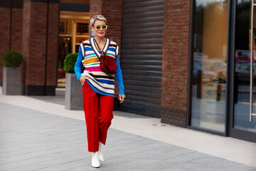 Fashionable Woman wearing trendy outfit, red trousers, blue jacket, striped vest, white shoes and...