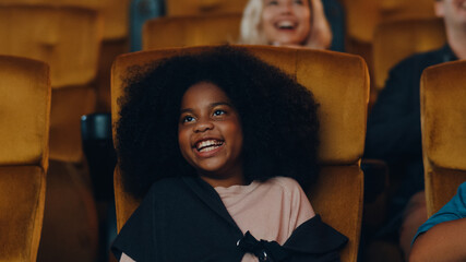 Attractive cheerful young black african girl laughing while watching film in movie theater....