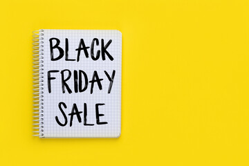 Black Friday Sale sign on open spiral notebook or notepad on bright yellow background, top view, flat lay with copy space. Shopping concept