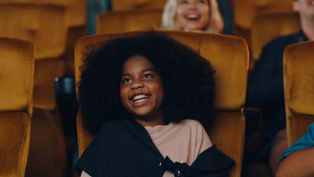 Attractive cheerful young black african girl laughing while watching film in movie theater. Lifestyle entertainment concept.