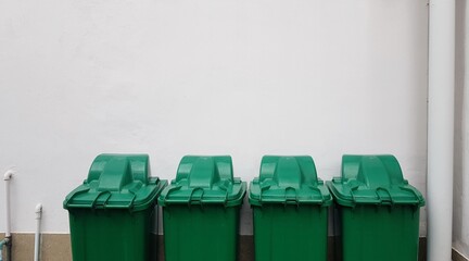 Four green trash bins placed against the wall of a white building.