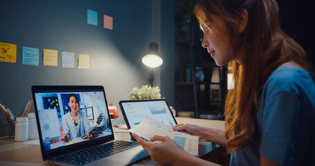 Asia woman using laptop talk to colleagues about work in video call while working from home at...