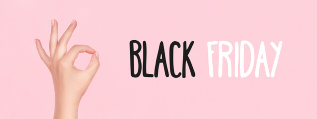 Black Friday sign on pink background with female hand with beautiful manicure - pink nude nails making ok sign, wide panoramic banner with copy space. Shopping concept