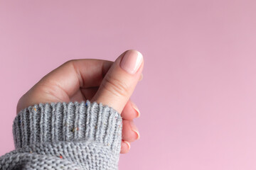 Obraz premium Female hand in gray knitted sweater with beautiful manicure - pink nude nails on pink background. Nail care concept