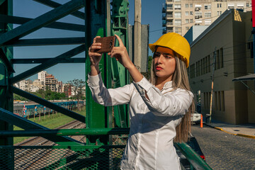 Beautiful young woman engineer or supervisor, taking a photo with her cell phone of the railway bridge she is inspecting. Concept of empowered woman, professional woman, professional job. technology.