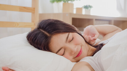 Beautiful attractive young Asian woman wake up, smiling and stretching her arms in her bed in bedroom. Young asia female use relax time at home. Lifestyle women relax at home concept.